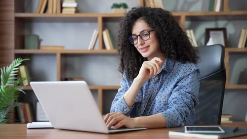 Young happy woman typing on a laptop while sitting at home office. Smiling beautiful female student