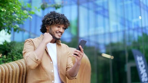 Man Cheers While Looking at Mobile Phone Outdoors