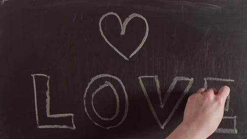 Hand Draws Heart and Word Love on Chalkboard