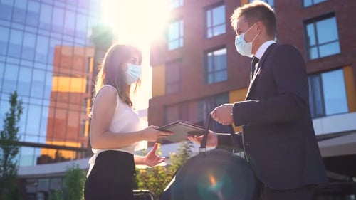 Side View of Cheerful Young Man and Woman in Formal Wear and Medical Masks Greeting