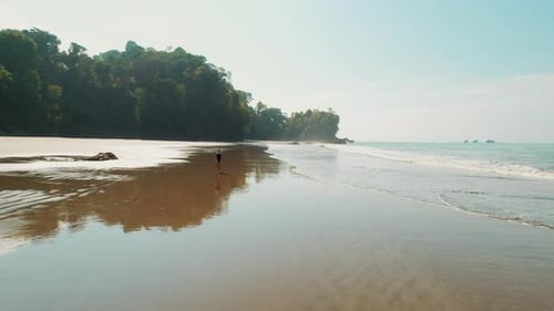 Tropical beach with lone woman walker at low tide on a sunny morning