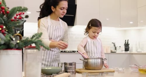 Mother and Her Little Child Daughter in Aprons Preparing the Dough in the Kitchen
