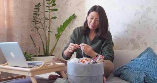Woman Crocheting at Home with Laptop Nearby