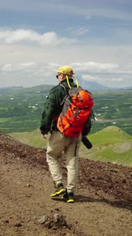 Solo Hiker with Bright Orange Backpack Walking Along a Mountain Trail Exploring Vast Green Highlands