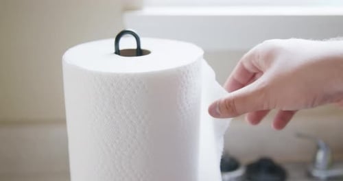 Hand Pulling Paper Towel from Roll Near Sink in Kitchen