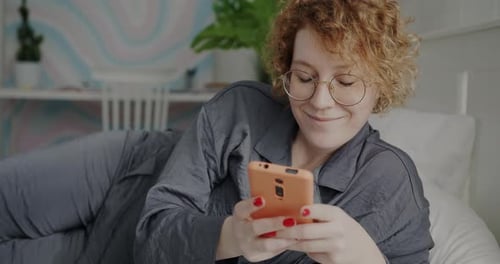 Woman Uses Phone While Lying in Bed Smiling