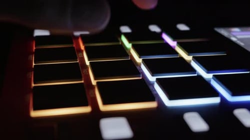 Productor musical creando un ritmo en un controlador Midi Pad iluminado en Dark Studio