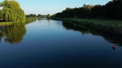 Tiefflug über langsam fließendem Wasser in einem Fluss, der die umgebende Vegetation widerspiegelt. Boot nähert sich