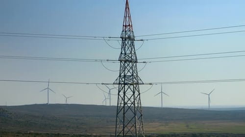 Hochspannungsleitung gegen rotierende Windmühlen und Windturbinen im Tal