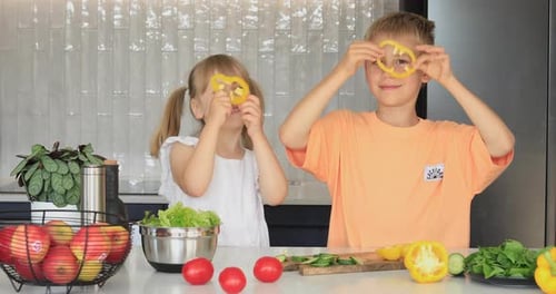 Brother and Sister Have Fun in the Kitchen and Put Pepper Rings on Their Eyes