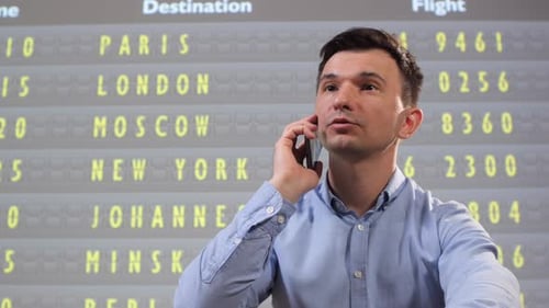 Man in Business Attire Talks Urgently on Smartphone at an International Airport Terminal Gesturing