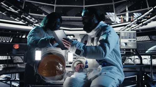 Astronaut Reviewing Onboard Analytics on Tablet Talking to Colleague