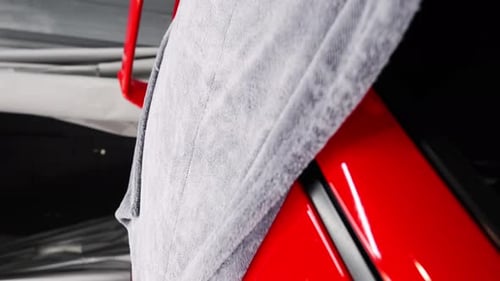 Man washes a red car, wipes water from the roof of the car with a microfiber towel. Car wash or car