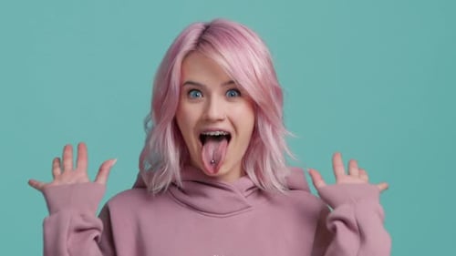 Hermosa chica despreocupada con cabello rosado mostrando la lengua extendida con las manos arriba