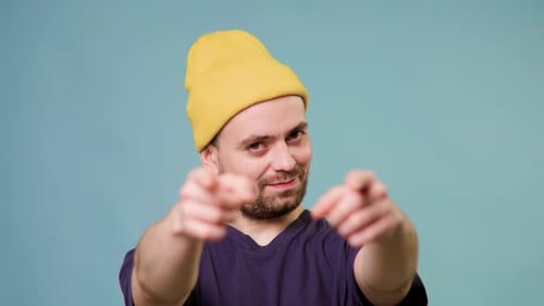 Young Adult Points Towards Camera Wearing Yellow Beanie