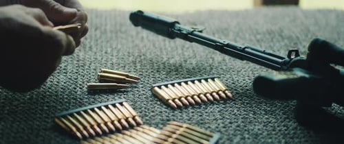 Person Prepares Bullets with Firearm on Gray Surface
