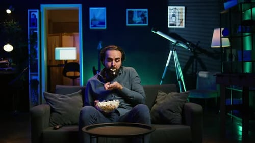 Un homme dans un appartement mangeant du pop-corn en regardant un film à la télévision