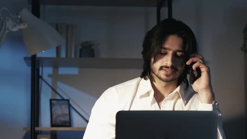 Man Talks on Phone and Uses Laptop at Night