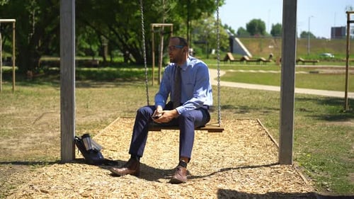 Unhappy, Sad Businessman Listen Music on Swing in City Park Attractive