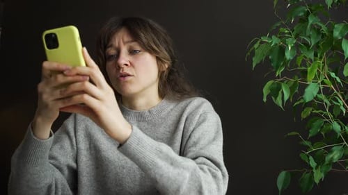Woman Uses Smartphone with Concerned Expression Indoors