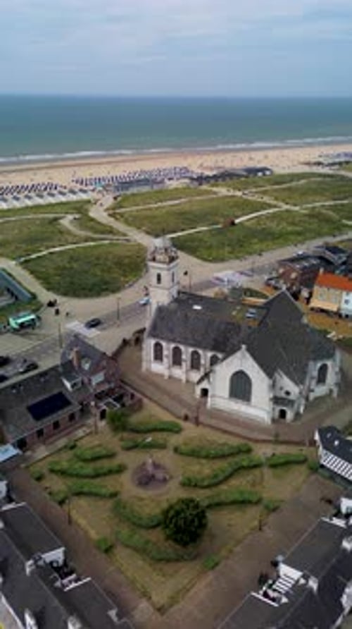 A scenic aerial view of a Dutch coastal town featuring a historic church, red-roofed houses red bus
