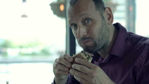 Handsome young man enjoys delicious burger during lunch break in city cafe