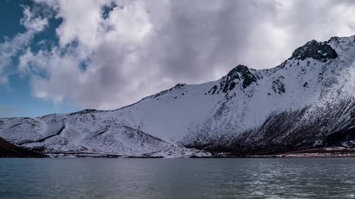 Dramatic Snowy Mountain Range Over Cold Lake Under Cloudy Sky