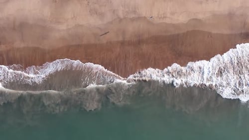 Abstract top-down aerial view of ocean waves breaking on a sandy beach, creating intricate white