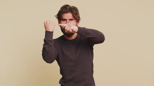 Portrait of Furious Young Indian Man Hits Fist on Palm Showing Fight Gesture Over Beige Background