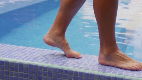 Nahaufnahme von Füßen, die am Pool spazieren gehen und den Zeh ins Wasser tauchen