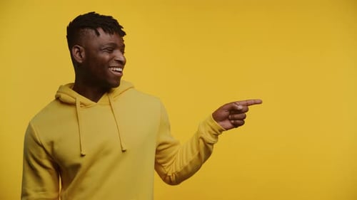 Joyful Man Pointing to the Side at Copy Space on Yellow