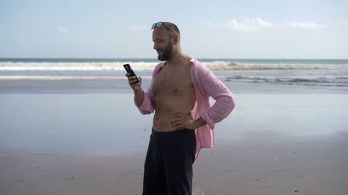Happy handsome man talks on cellphone while standing on a sunny beach