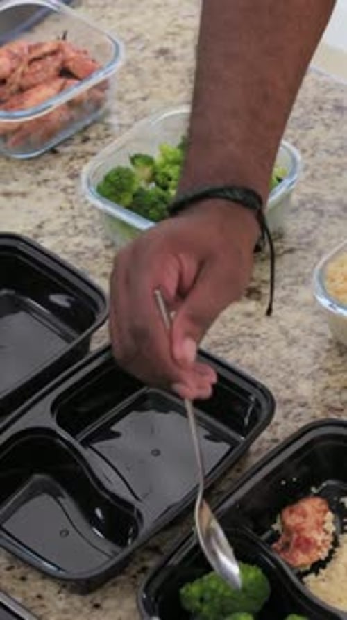 Vidéo verticale : Cueillette de brocoli à bras ouverts et ajout de poulet sur le plan de travail de la cuisine avec des plateaux vides et une cuillère
