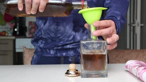 Um homem derrama vodka com infusão de flores de lavanda em uma garrafa de vidro.