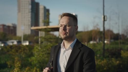 A Satisfied Elegant Man in Glasses Walks Through a City Park The Man is Wearing a Stylish Coat and