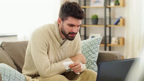 Man With Tissue Sitting on Couch Using Laptop