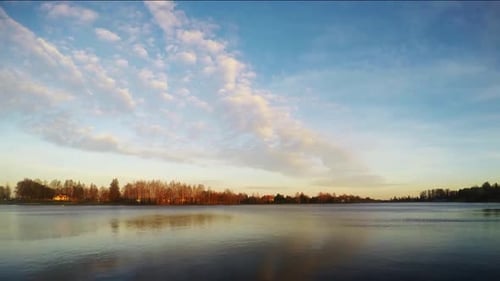 Sunset clouds over the river and trees without leaves. Time lapse