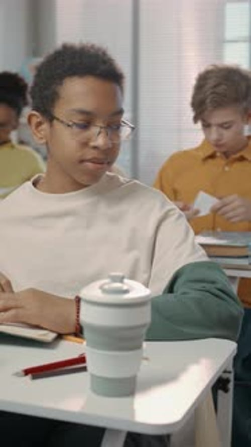 Black Teenage Boy Sitting at Desk Recieving Paper Note from Classmate