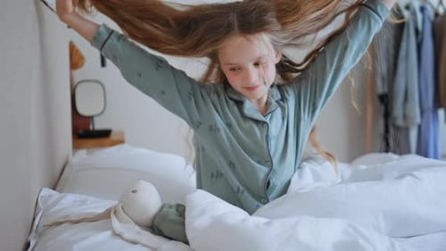 Girl Sitting in Bed Playing with Hair and Toy