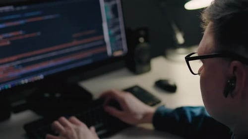 A Young Middle Aged Programmer Works Remotely In His City Apartment At Night. It Specialist Sits