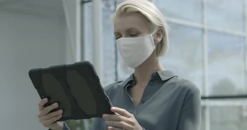 Business woman wearing face mask and working on digital tablet in office lobby