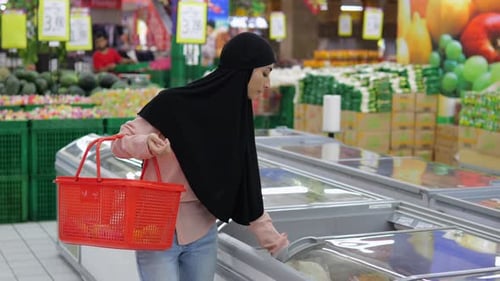 Woman in a Supermarket Takes Frozen Products From the Freezer and Puts Them in Her Red Shopping