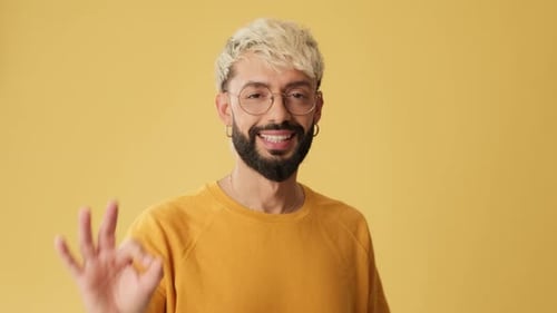 Close up, man showing ok gesture, looking at camera isolated on yellow background in studio