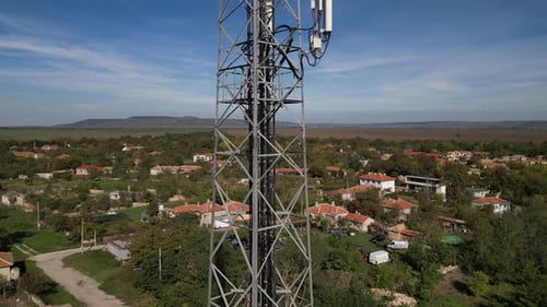 Closeup of a Telecommunications Tower in a Rural Area with a Village and Fields in the Background