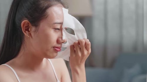 Close Up Of Asian Woman Taking Off Sheet Facial Mask, Touching Her Face And Smiling