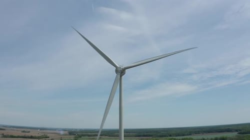 Close up aerial view of windmill blades turning in the breeze against blue sky with soft thin white