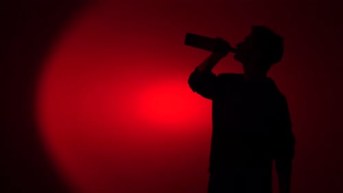Silhouette of young man drinking from a bottle