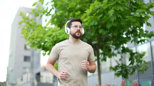Male runner jogging in urban city street. Handsome active man with wireless headphones enjoys joggin