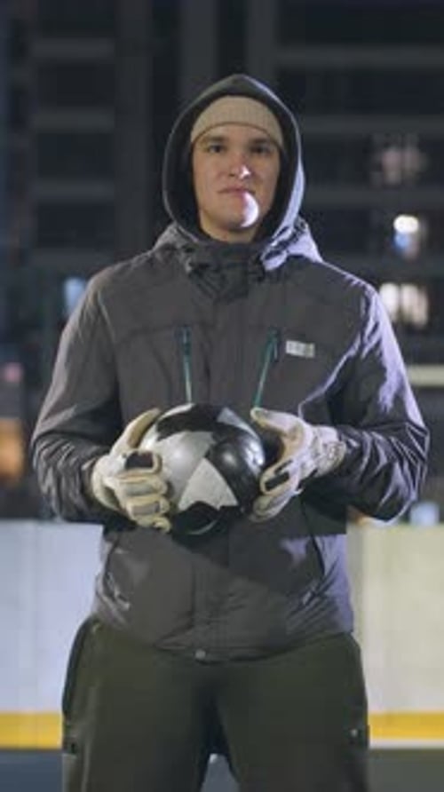 Thoughtful Man Holding Soccer Ball on Urban Sports Field at Night