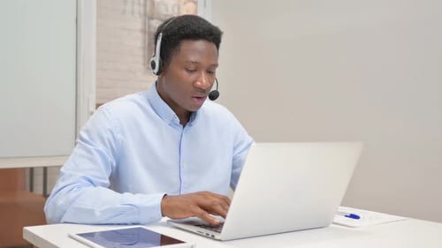 African Man with Headset Doing Video Chat on Laptop in Call Center